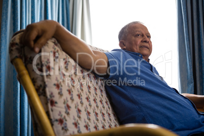 Senior man looking away while relaxing on sofa at retirement home