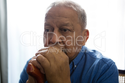 Thoughtful sad senior man holding walking cane while sitting on chair