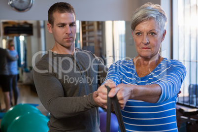 Male physiotherapist helping patient in performing exercise with resistance band