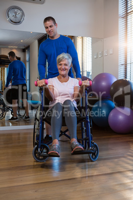 Male physiotherapist helping patient in performing exercise with dumbbell in clinic