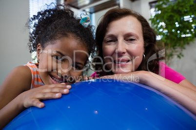Portrait of smiling girl and physiotherapist leaning on fitness ball