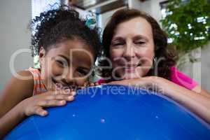 Portrait of smiling girl and physiotherapist leaning on fitness ball