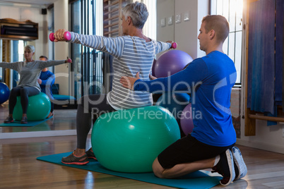 Physiotherapist assisting senior woman on exercise ball and dumbbells