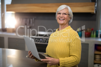 Senior women holding a laptop while standing in the kitchen