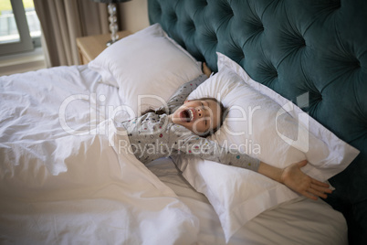 Girl yawning while stretching her arms in bed