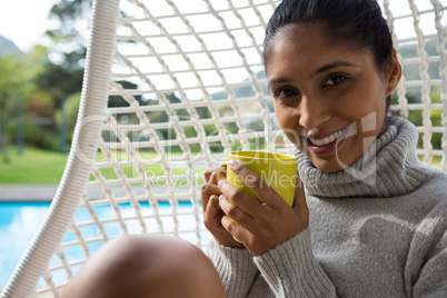 Portrait of woman with coffee cup resting in swing chair