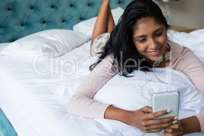 Smiling woman using phone on bed