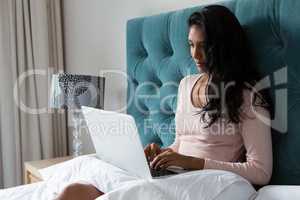 Woman using laptop on bed at home