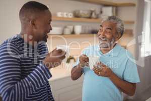 Smiling father and son interacting while having cup of coffee