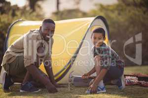 Smiling father and son pitching their tent in park
