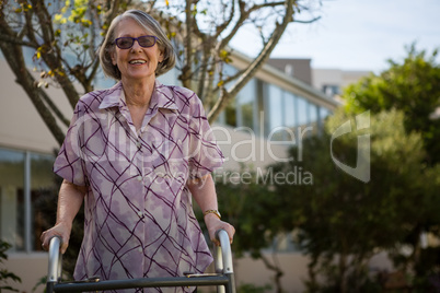 Happy senior woman holding walker while standing in yard