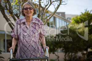 Happy senior woman holding walker while standing in yard