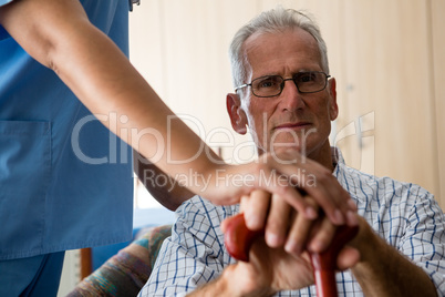 Female doctor standing by senior man sititng on sofa in retirement home