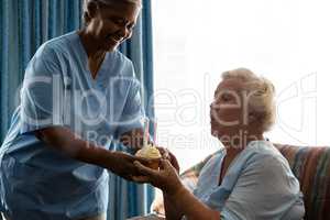 Senior woman blowing candles of cup cake being held by nurse