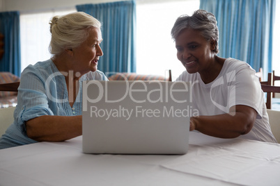 Senior woman showing laptop to friend at table