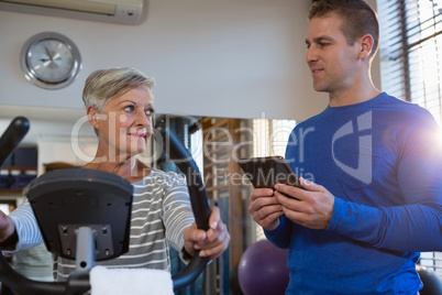 Physiotherapist interacting with senior woman while exercising on exercise bike