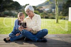 Granddaughter and grandmother using a digital tablet in the deck shade
