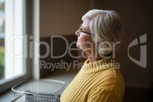 Thoughtful senior woman looking through kitchen window