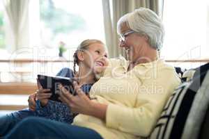 Smiling granddaughter and grandmother using digital tablet on sofa