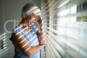 Tense senior woman standing near window in bedroom