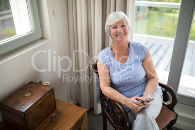 Smiling senior woman sitting on chair with mobile phone