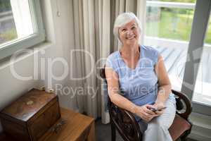 Smiling senior woman sitting on chair with mobile phone