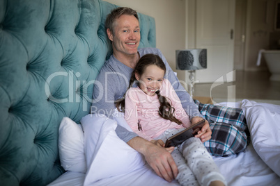 Smiling father and daughter using digital tablet on bed