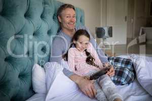 Smiling father and daughter using digital tablet on bed
