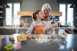 Grandmother helping granddaughter to flatten dough