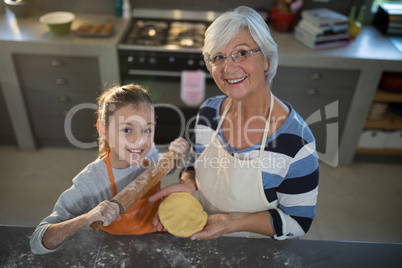 Grandmother and granddaughter posing while holding dough and rolling pin