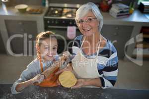 Grandmother and granddaughter posing while holding dough and rolling pin