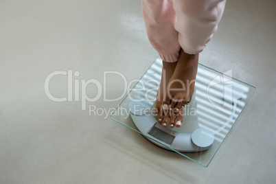 Low section of woman standing on bathroom scale