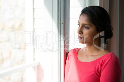 Thoughtful young woman looking through window