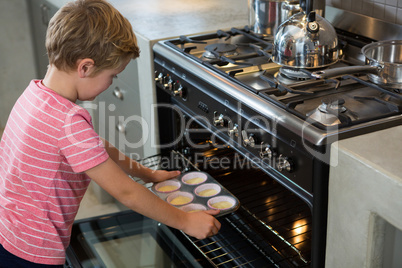 Boy holding muffin tin by oven in kitchen