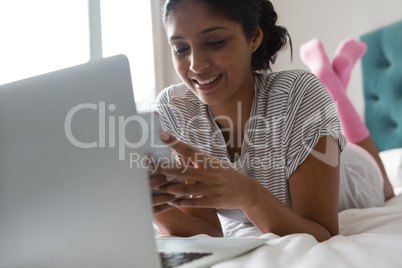 Smiling woman with laptop using phone on bed