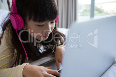 Girl listening to music while using laptop on bed