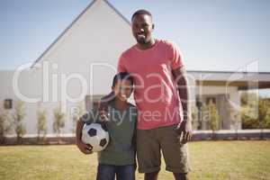 Smiling father and son standing in garden with football