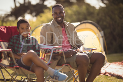 Smiling father and son sitting on chair in park