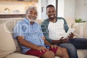 Smiling father and son sitting on sofa with digital tablet in living room