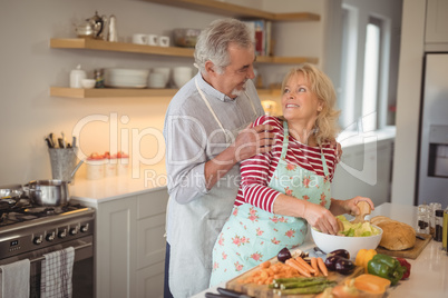 Senior couple looking at each other while mixing vegetables in kitchen