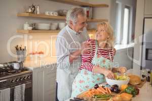 Senior couple looking at each other while mixing vegetables in kitchen