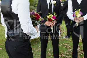 Bridegroom and best man standing with bouquet of flowers in garden