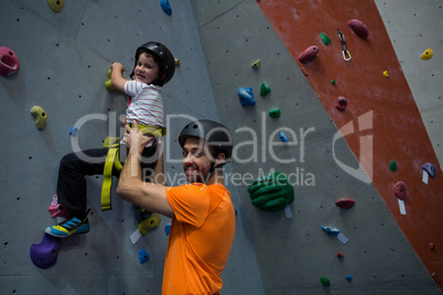 Trainer assisting boy in rock climbing