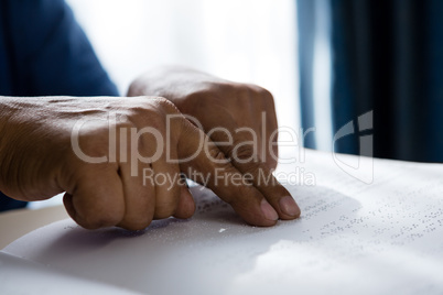 Cropped hands on senior man reading braille book in retirement home