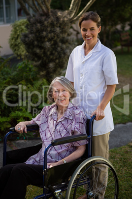 Smiling doctor standing by senior woman sitting on wheelchair in park