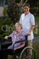 Smiling doctor standing by senior woman sitting on wheelchair in park