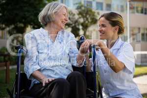 Doctor talking to woman sitting on wheelchair in park