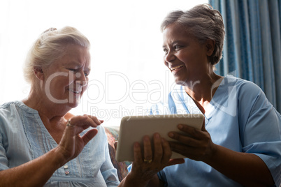 Cheerful senior woman with doctor using digital tablet while sitting on sofa