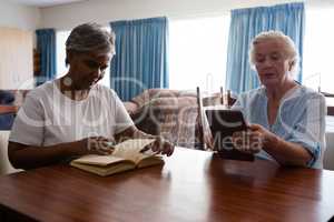 Woman reading book while friend using tablet at table
