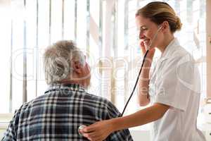 Female doctor examining senior patient with stethoscope